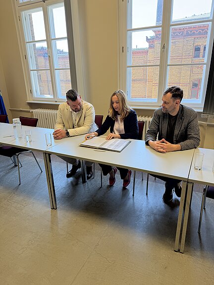 Mitarbeiter Team HOWOGE Schulbau sitzend in Klassenzimmer mit Vertragsunterschreibung