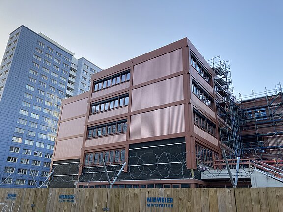 Blick auf die Fassade des Schulgebäudes und dahinter ein hohes Wohngebäude