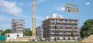 Ein Kran zieht eine Wand an einem Neubauprojekt hoch.