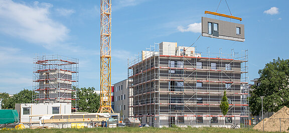 Ein Kran zieht eine Wand an einem Neubauprojekt hoch.