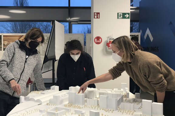 Drei Menschen betrachten ein Architekturmodell