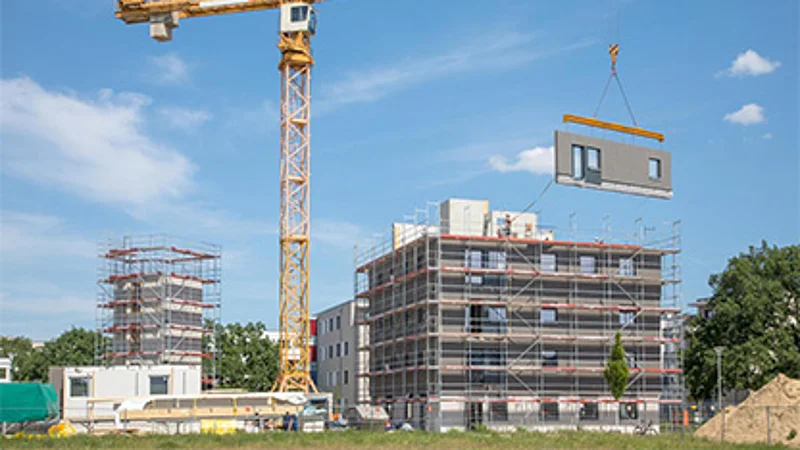 Foto eines Neubauprojektes in der Bauphase. Ein Kran hebt ein Modul für den Neubau hoch. 