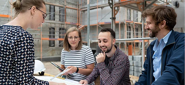 4 Azubis stehen vor einem Bauprojekt und besprechen sich.
