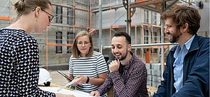 4 Azubis stehen vor einem Bauprojekt und besprechen sich.