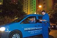 Das blaue Hausmeisterauto der HOWOGE mit einem Fahrer im Blaumann und ein weiterer hausmeister, der vor dem Auto steht.