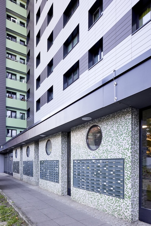 Nahaufnahme des Eingangsbereichs mit runden Fenstern und grobem Putz