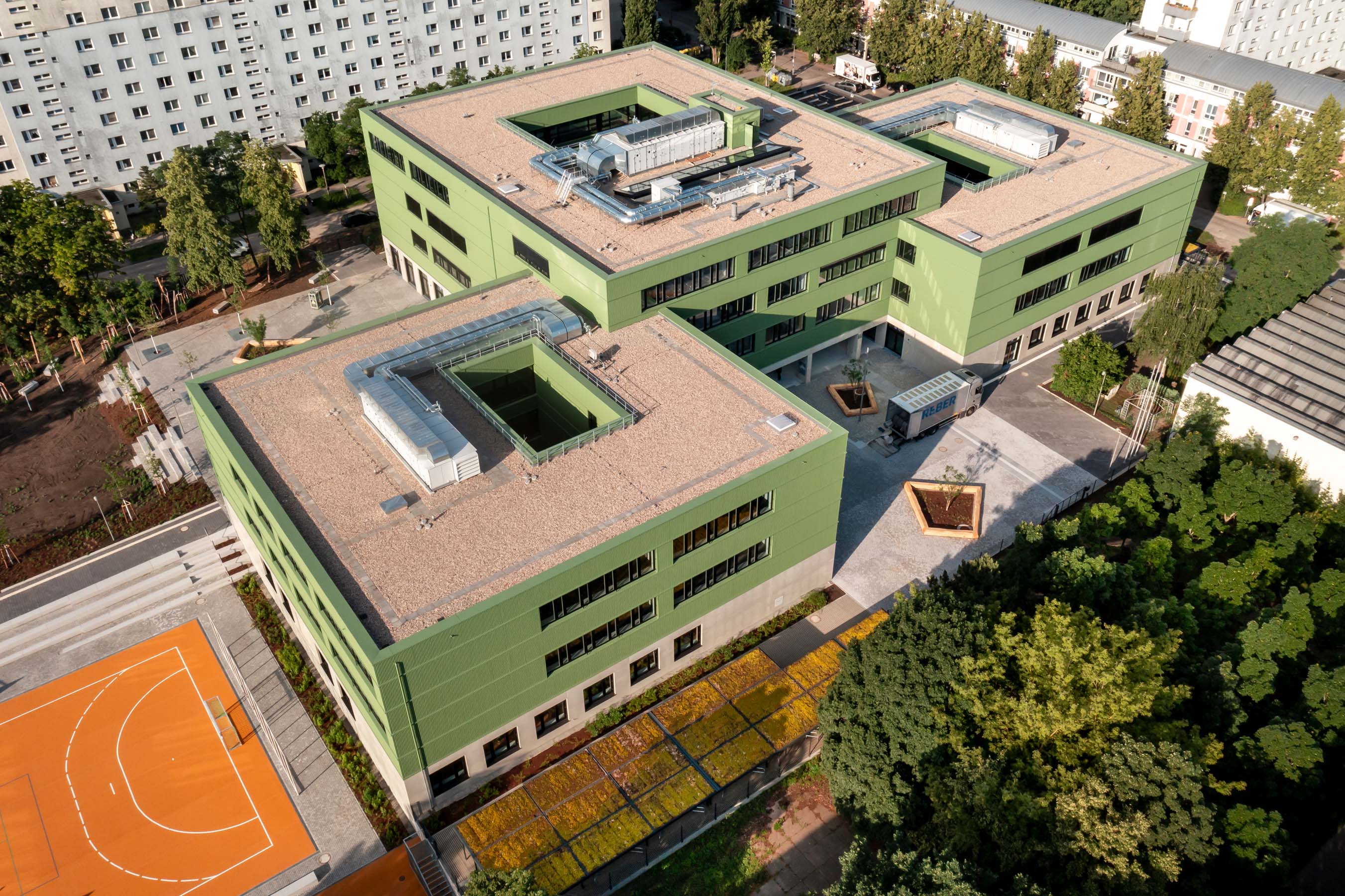 Vogelperspektive, Außenansicht grüne Fassade mit Schulhof und Basketballplatz