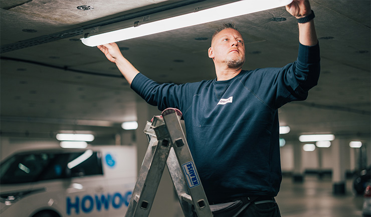 Ein Mitarbeiter der ATOZ Facility Solutions GmbH wechselt eine Lampe aus und steht dabei auf einer Leiter.