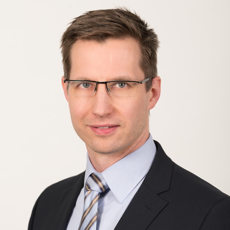 ein Mann mit Brille und Anzug schaut in die Kamera