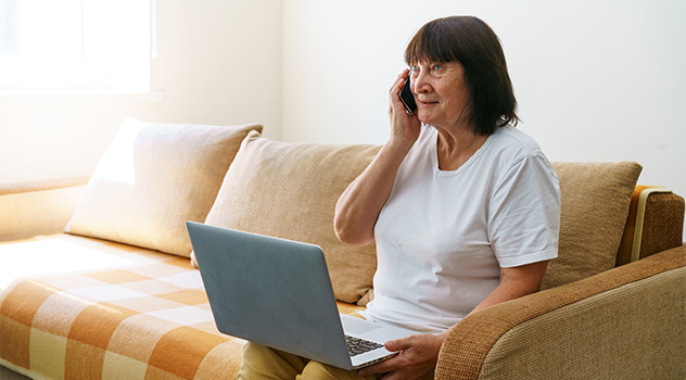Eine Frau mit einem Laptop auf dem Schoß und einem Smartphone in der Hand.
